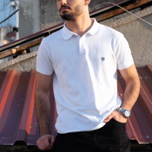 Portrait of a man in a white polo shirt posing on a rooftop. Bright sunlight highlights his features.
