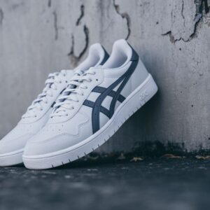 A pair of white and blue sneakers leaning against a textured concrete wall.